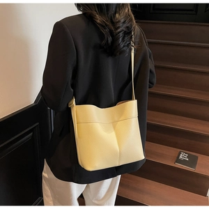 Detail of light yellow lychee grain leather bucket bag shown on model at wood staircase