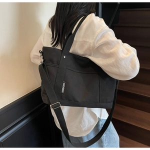 Side view of a black canvas tote bag with adjustable shoulder straps on a female model
