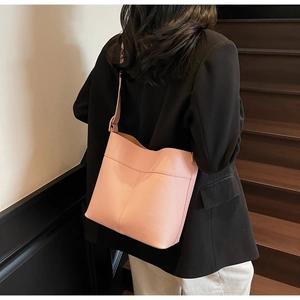 Close-up of pink litchi grain leather bucket bag with elegant stitching worn by a model