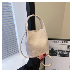 Detail of a creamy white bucket bag with pebble leather texture and elegant handles