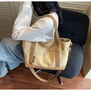 Detailed side view of a beige canvas tote bag with brown straps worn by a model