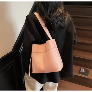 Detail of light pink bucket bag with wide strap worn by model on dark stairs