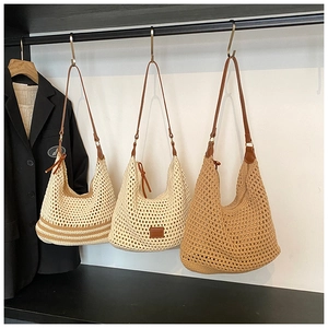 Three straw hobo bags with hollow woven design and brown leather straps hanging in a row