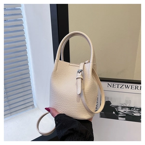 Detail of cream bucket bag showing lychee pattern leather texture and silver buckle