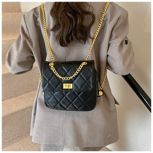 Detail of black quilted leather shoulder bag with gold chain strap on a model
