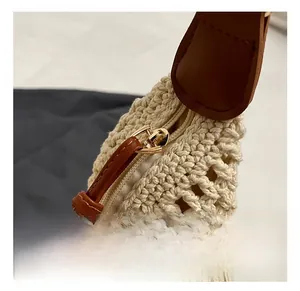 Detailed close-up of golden metal zipper and brown leather trim on beige knit tote bag