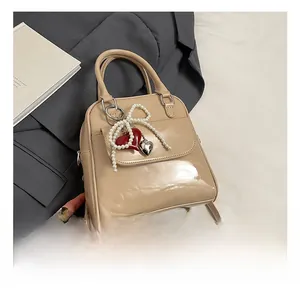 Detail of beige patent leather bag with pearl bow and heart charms on grey blazer