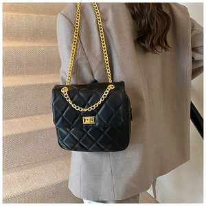 Detail of black quilted leather shoulder bag with gold chain strap on office outfit