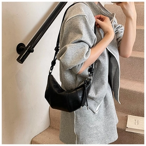 Detail of black glossy leather crescent bag with unique knotted strap and metal zipper