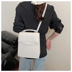Vertical rectangular white leather handbag with flap design and curved top handle shown on model