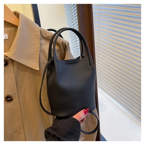 Detail of black pebbled leather bucket bag with top handle and shoulder strap on trench coat