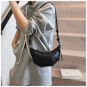 Detail of a minimalist black croissant bag made of matte leather worn by a model