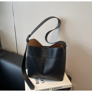 Close-up of black lychee grain leather bucket bag with adjustable strap on a prop book