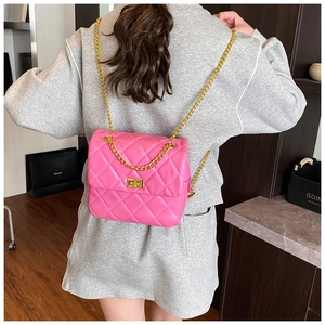 Macro detail of vibrant pink quilted bag with gold chain strap on a grey outfit