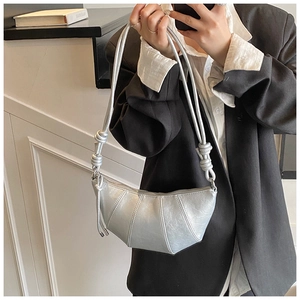 Macro view of silver crescent bag with metallic pleated texture and knotted shoulder strap