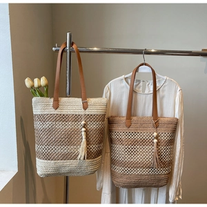 Détail de sacs cabas en paille avec bandoulières en cuir et pompons décoratifs en bois