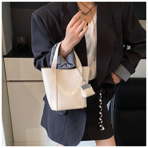 Detail of a creamy white glossy tote bag with a matching mini charm held by a model
