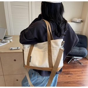 Detail of beige canvas tote bag with brown straps and side pockets on office desk