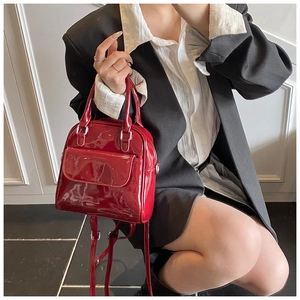 Side view of a glossy red patent leather mini backpack with top handles and shoulder straps