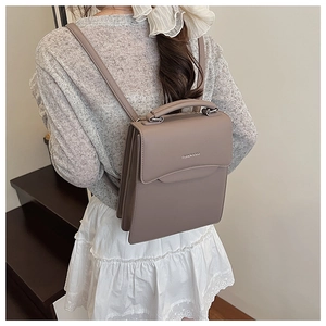 Detailed back view of a grey versatile handbag worn by a model in an indoor setting