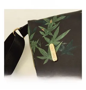 Close-up of golden metal zipper and brand plate on waterproof nylon leaf print bag