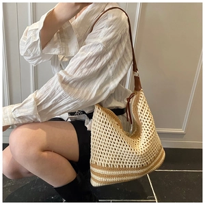 Hollow straw shoulder bag with brown leather strap worn by a model against a wall