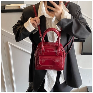 Close-up of a glossy red patent leather handbag with a top handle and shoulder strap