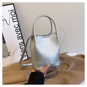 Close-up of silver bucket bag with litchi grain texture on brown fabric backdrop