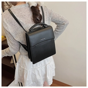 Detail of a minimalist black PU leather handbag with silver logo and top handle strap