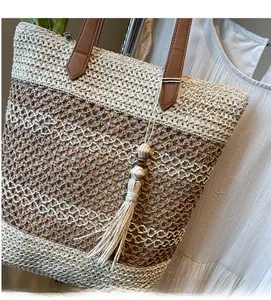 Détail du sac cabas en paille avec design à étages et breloque bohème à pompons