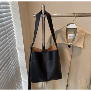 Detail of black pebbled leather bucket bag hanging with wide shoulder strap on a rack