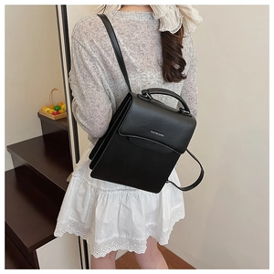 Close-up of black matte leather handbag with adjustable straps and fashion text detail