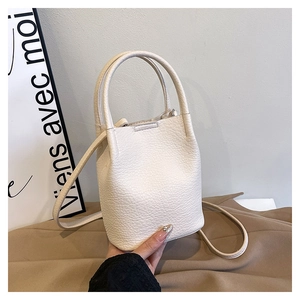 Close-up of beige bucket bag with lychee texture and slim shoulder strap detail