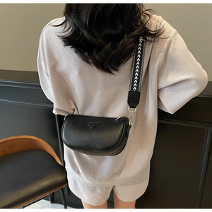 Detail of black semi-circle crossbody bag with wide geometric strap worn by model