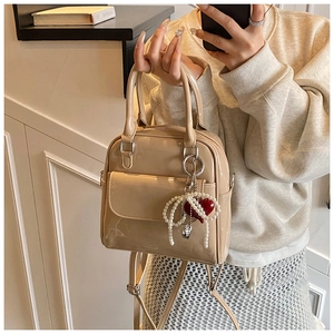 Detail of beige patent leather mini backpack featuring pearl and red heart charm accessories