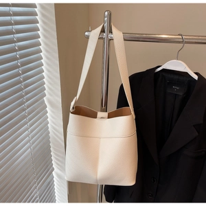 Detail of off-white lychee leather bucket bag hanging on silver stand with soft light