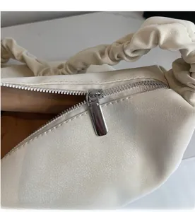 Close-up of smooth silver metal zipper and pleated handle on off-white tote bag