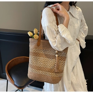 Détail d'un sac cabas en paille avec anses en cuir marron et pendentif décoratif en bois