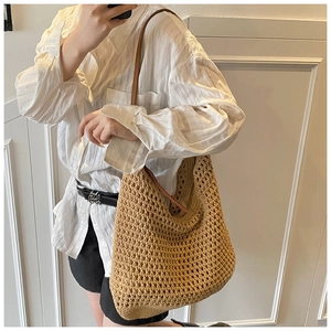 Detail of hand-woven straw tote bag with brown leather strap in bohemian style