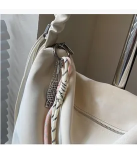 Detail of cream hobo bag with trendy tennis racket pendant and braided charms