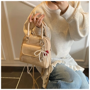 Detail of beige patent leather bag with pearl bow and cherry charm pendant