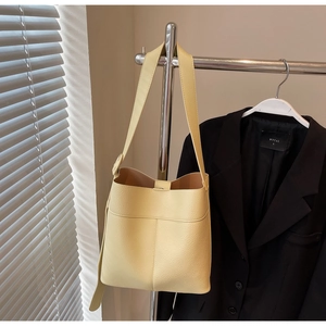 Detail of light yellow lychee pattern bucket bag with adjustable strap on a metal hanger