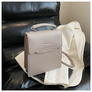 Detail of khaki leather handbag featuring metal lettering on black leather sofa setting