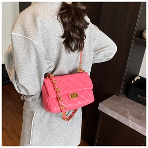 Detail of bright pink quilted crossbody bag with gold chain strap worn by a model