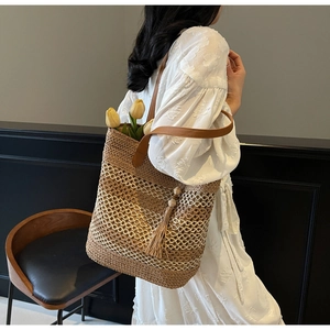 Détail d'un sac cabas en paille avec résille blanche, glands et anses en cuir marron