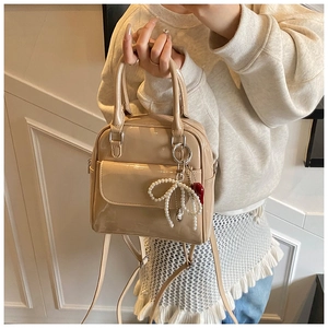 Detail of glossy beige patent leather mini backpack with pearl bow charm and top handle