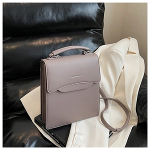 Chic taupe square leather handbag with double curved flap on a designer sofa setup
