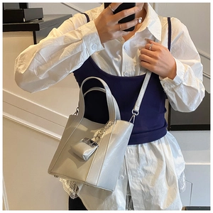 Close-up of a light grey bucket bag with metal chain and matching micro pendant charm