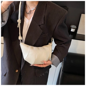 Detail of a beige crescent crossbody bag with pleated seams and knot strap on a model