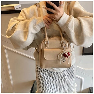 Detail of beige patent leather mini square bag featuring a pearl heart charm accessory